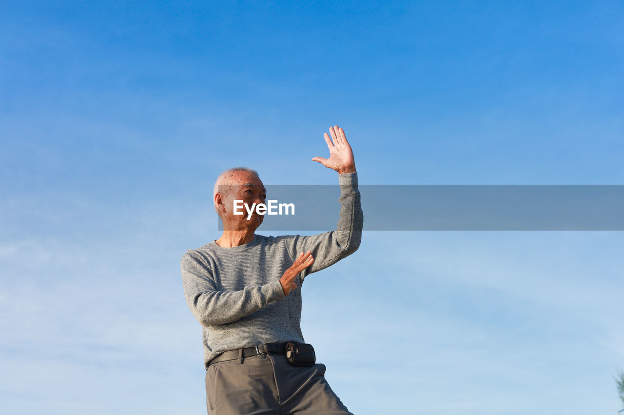 Man gesturing while standing against sky