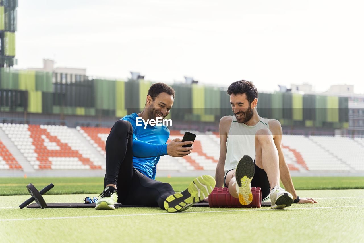 Smiling friends looking at mobile phone while sitting outdoors