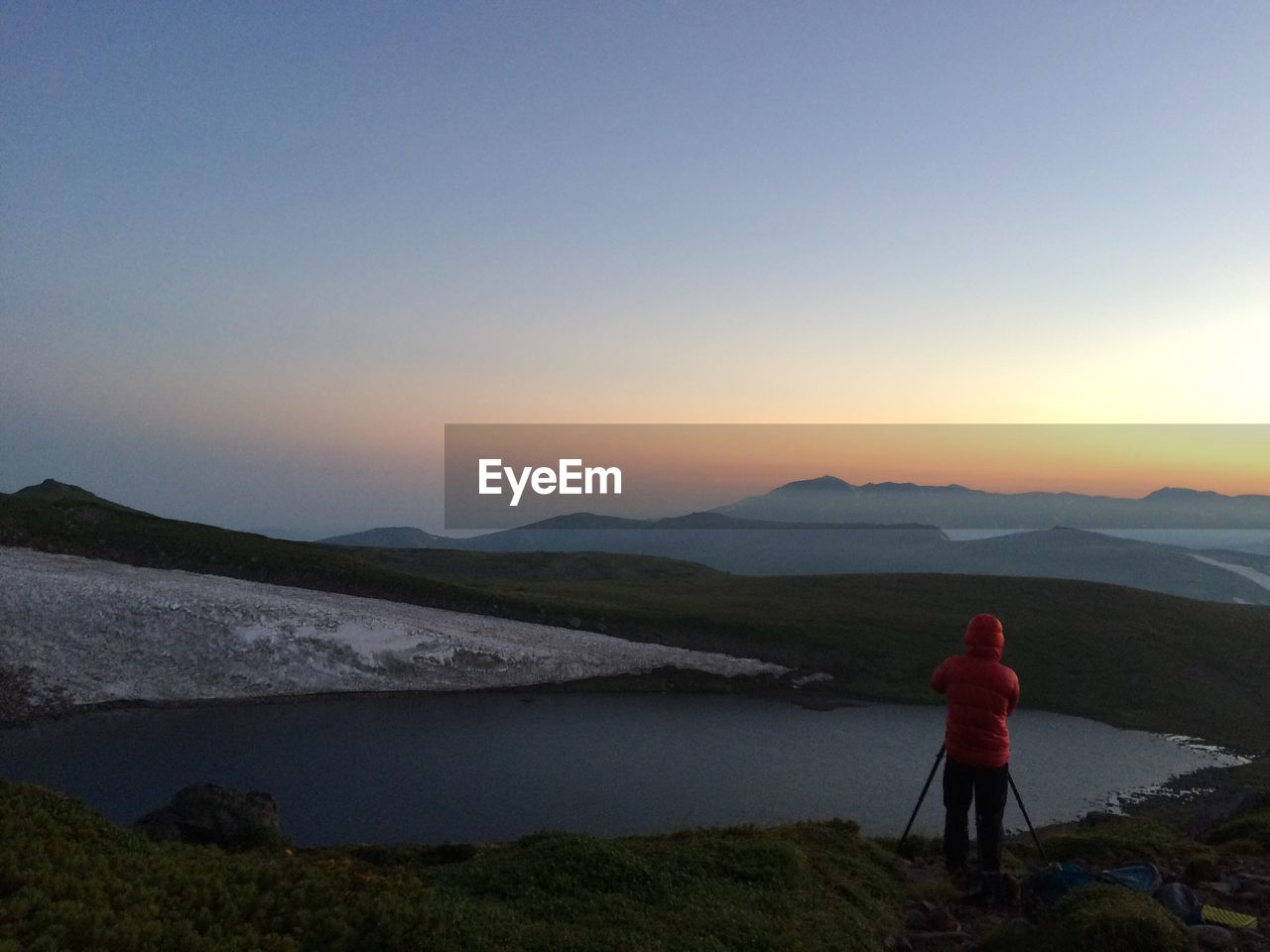 Rear view of woman photographing lake against clear sky during sunset