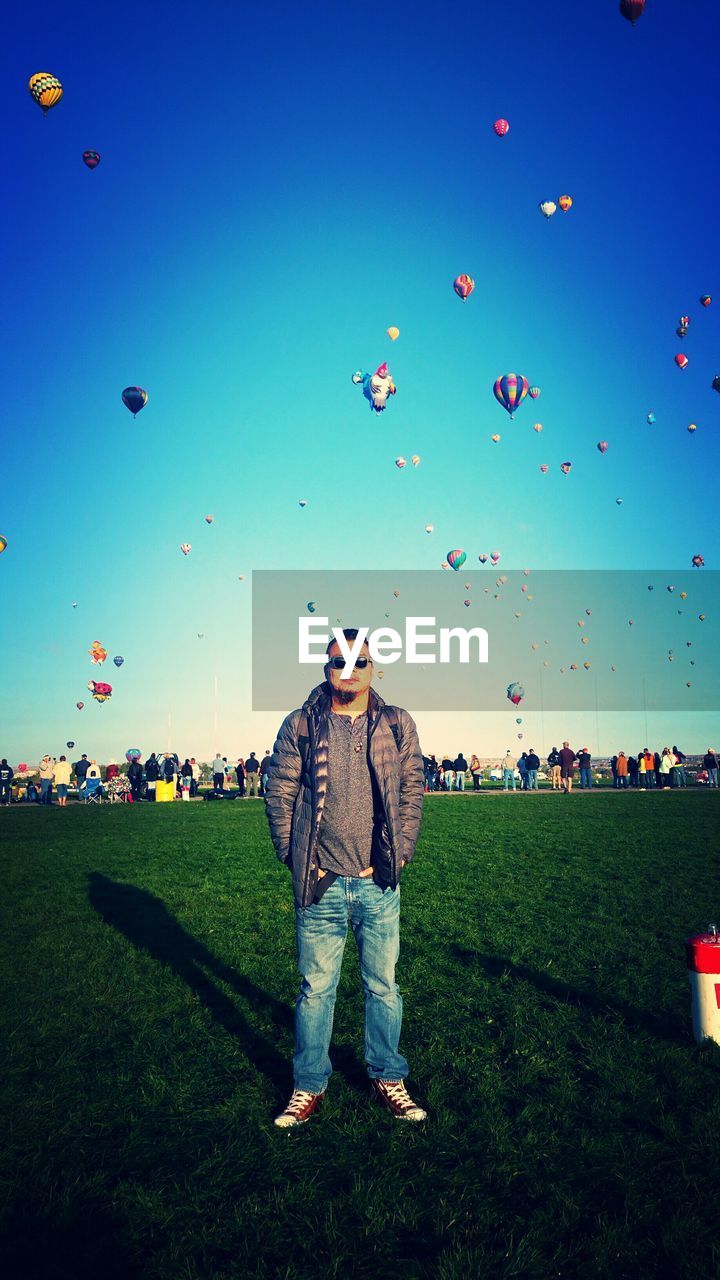 Portrait of man standing on field against hot air balloons in sky
