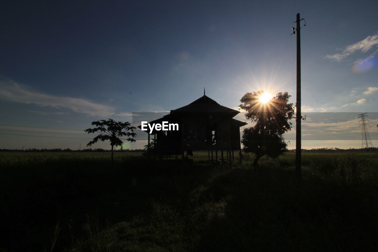 Silhouette built structure on field against sky at sunset