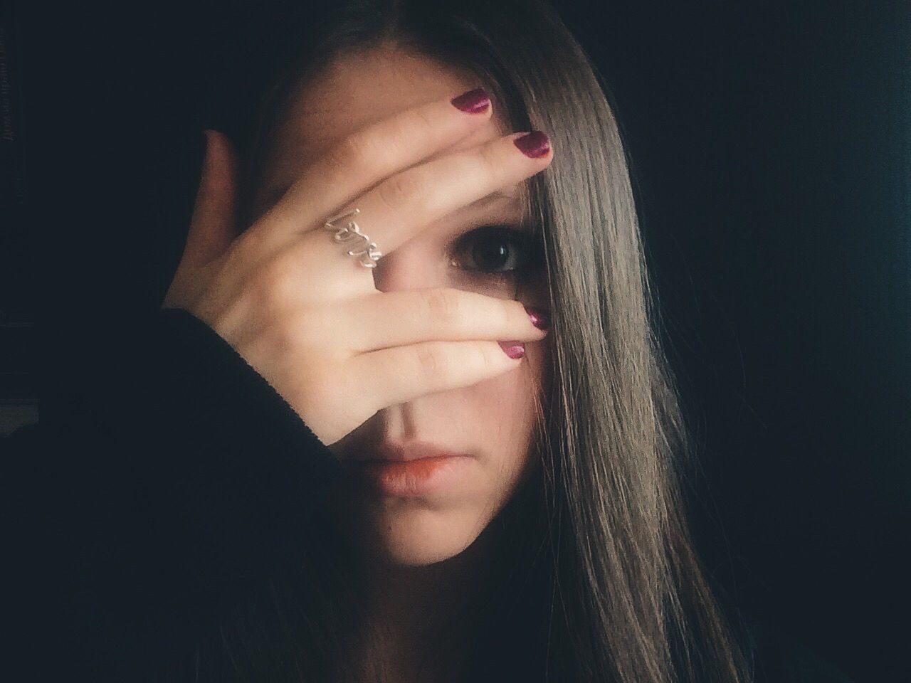 Close-up of woman looking through fingers with love text ring against black background