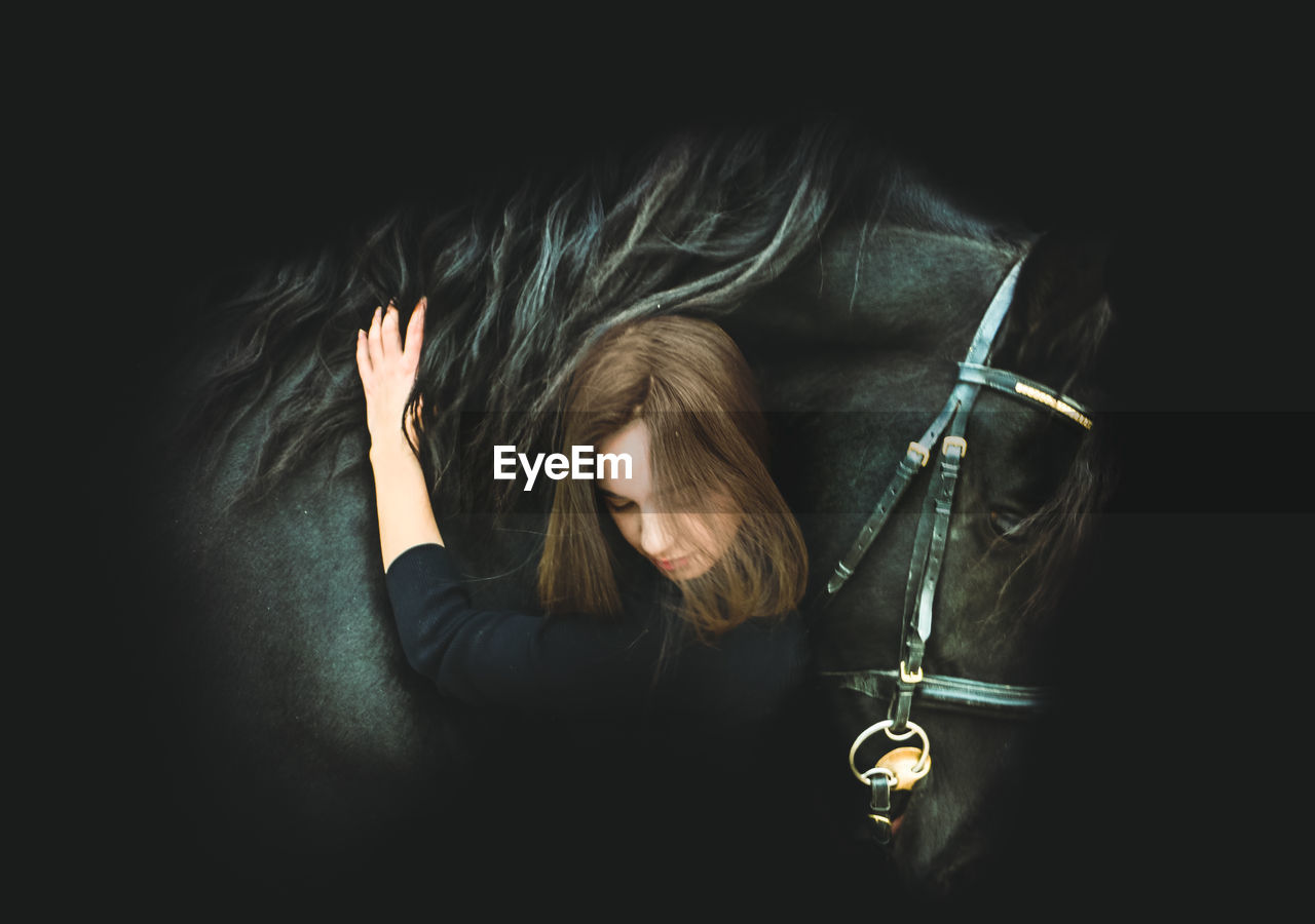 Digital composite image of woman embracing horse against black background