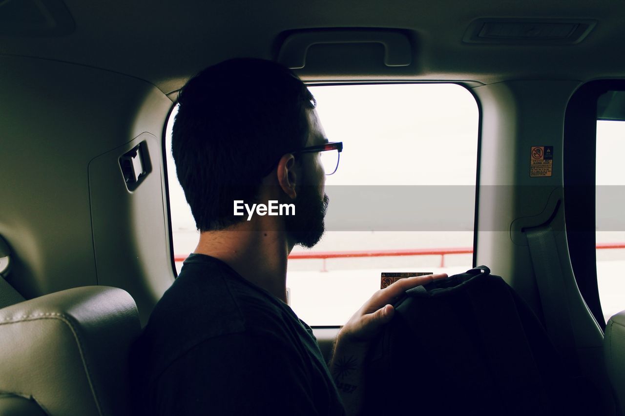 Side view of man with eyeglasses sitting in car looking outside window