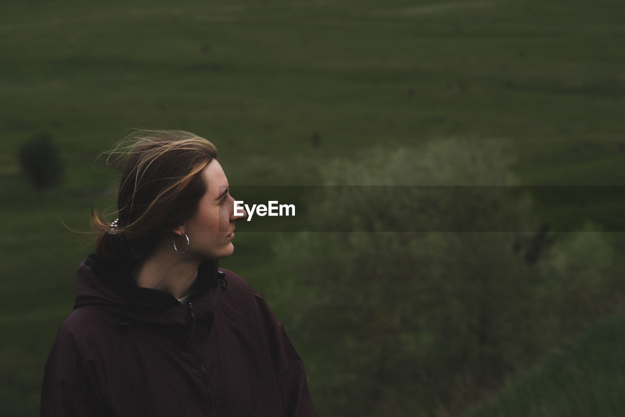 Woman in a rain anorak stands on the hill, deep green background. 