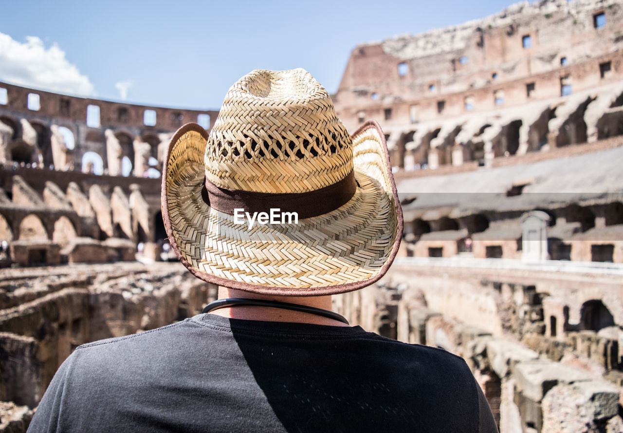 Rear view of mid adult man wearing hat standing against old ruins