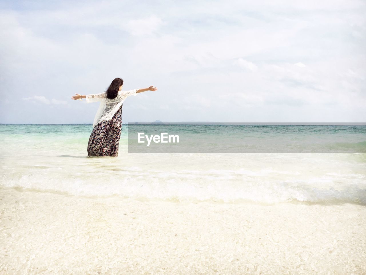 Rear view of woman with arms outstretched standing on shore against sky