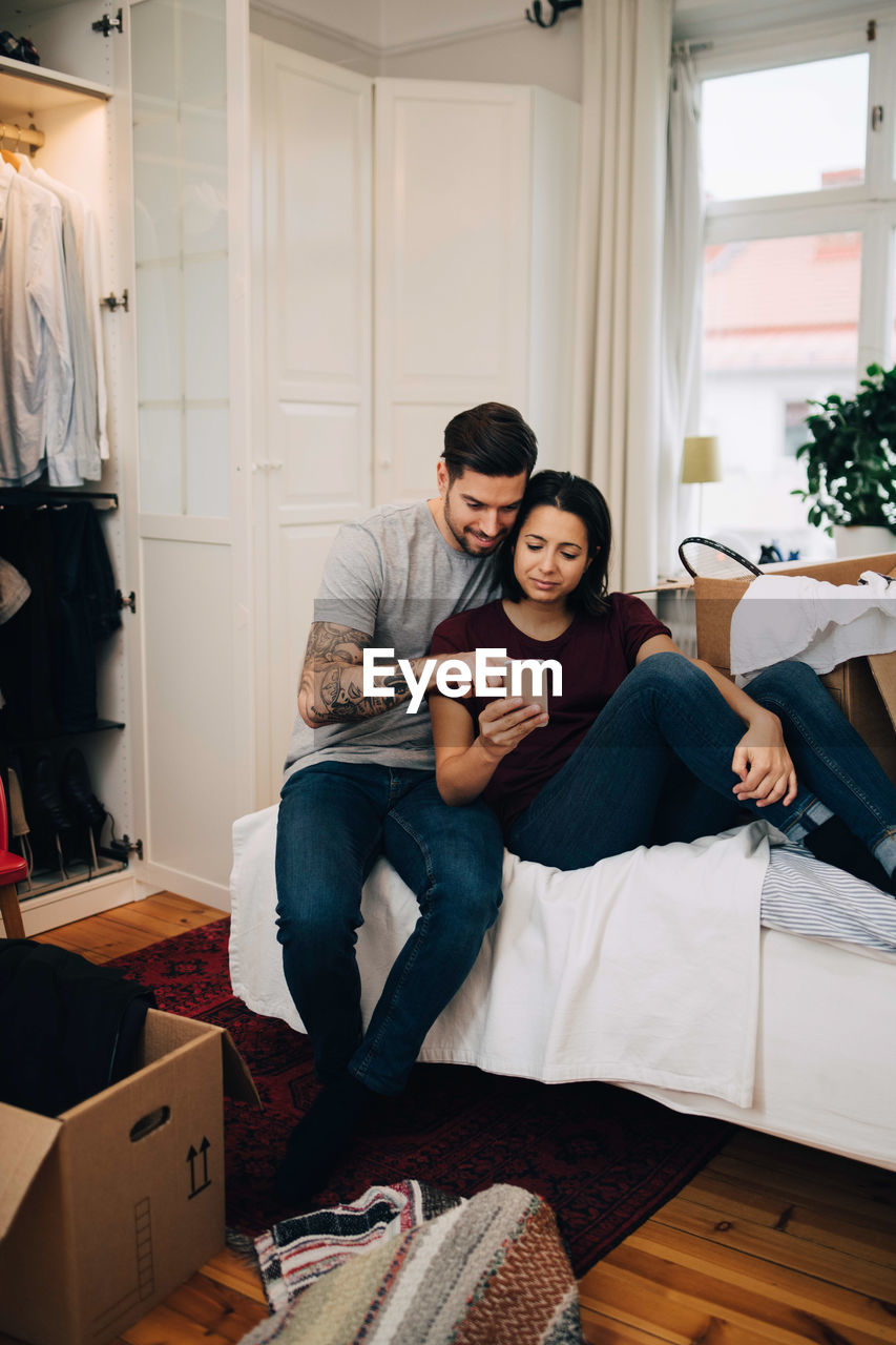 Couple using mobile phone while resting on bed in bedroom