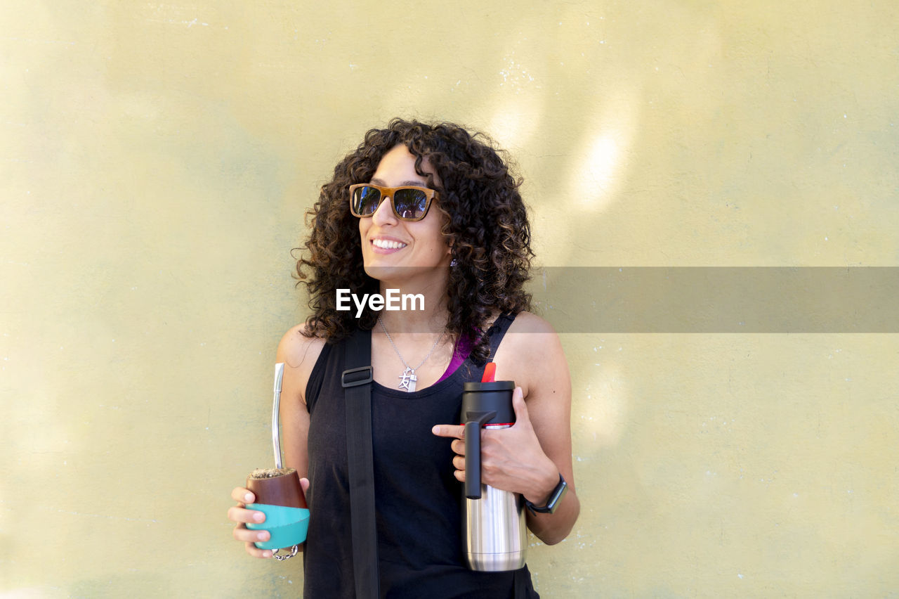 Mixed race woman smiling while drinking mate outdoors.