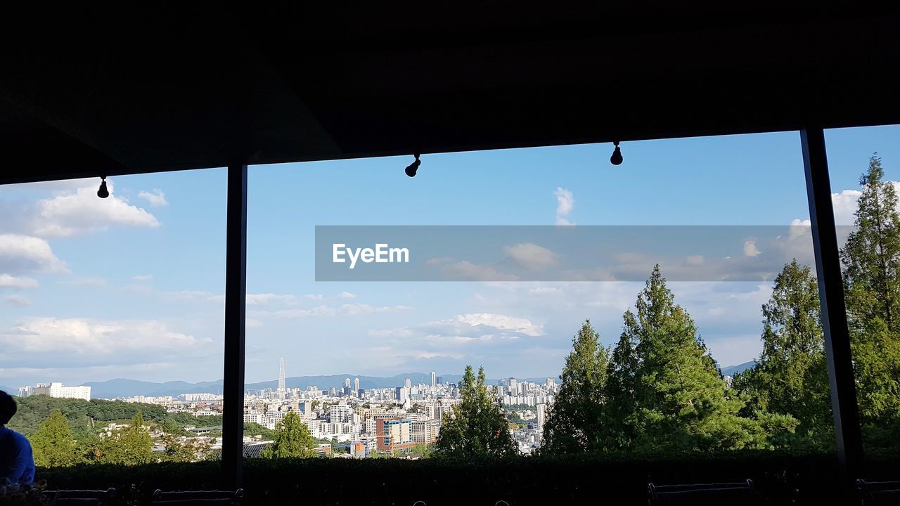 TREES AND BUILDINGS AGAINST SKY SEEN THROUGH WINDOW