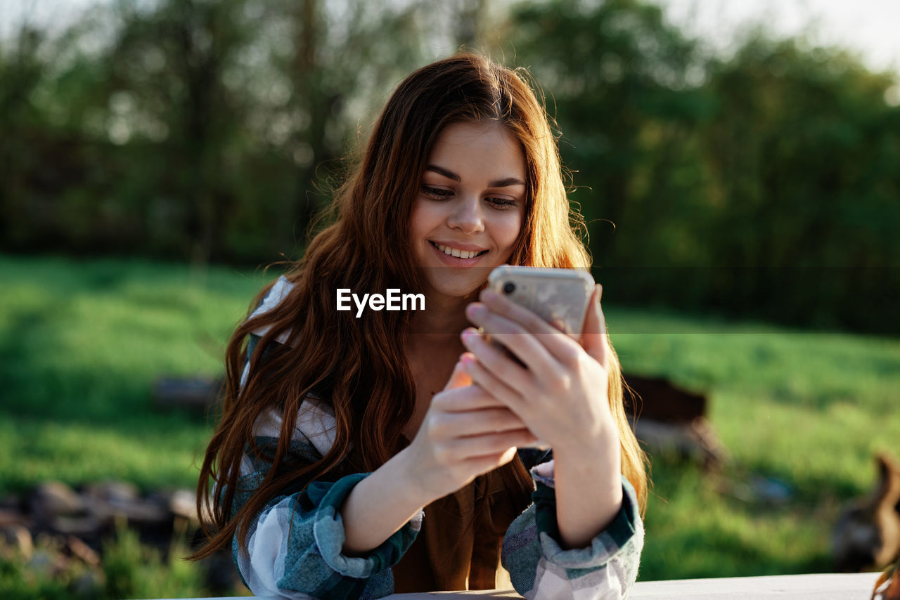 young woman using phone while sitting on field