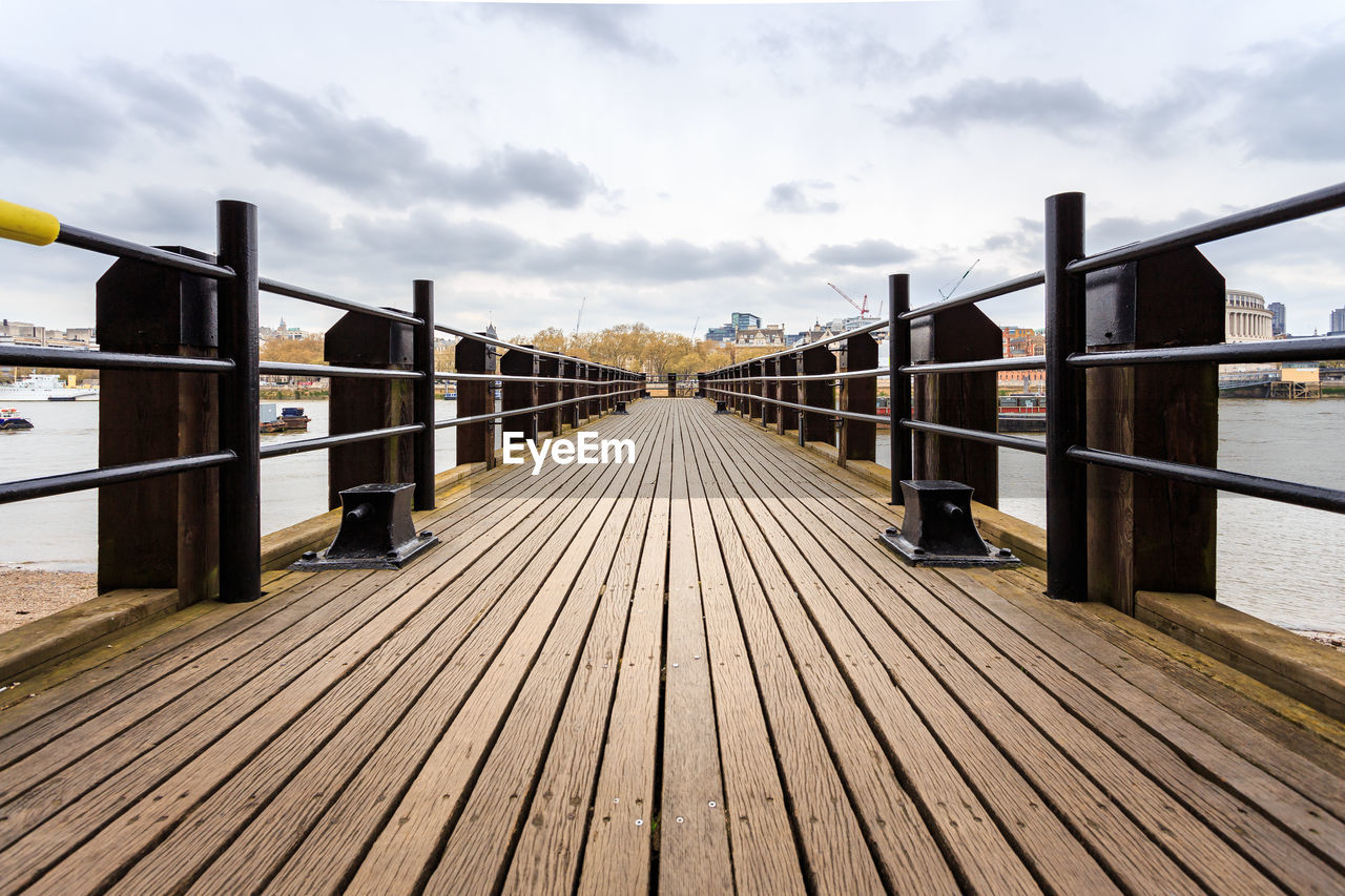 Pier on footbridge over river against sky