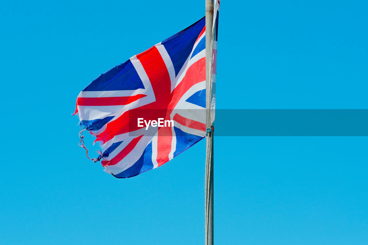 Low angle view of tattered flag of the uk against blue sky