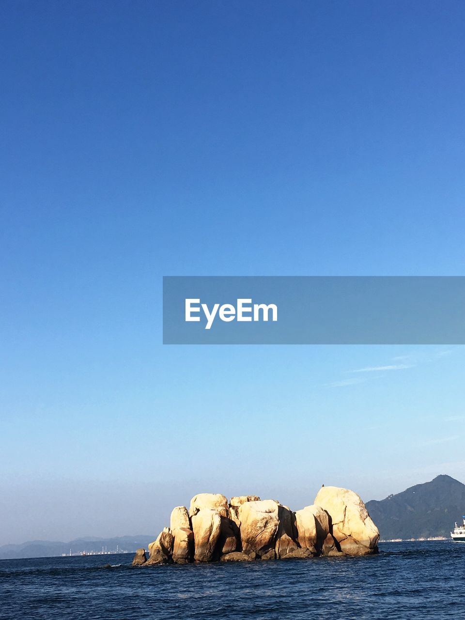 Rock formation in sea against clear blue sky