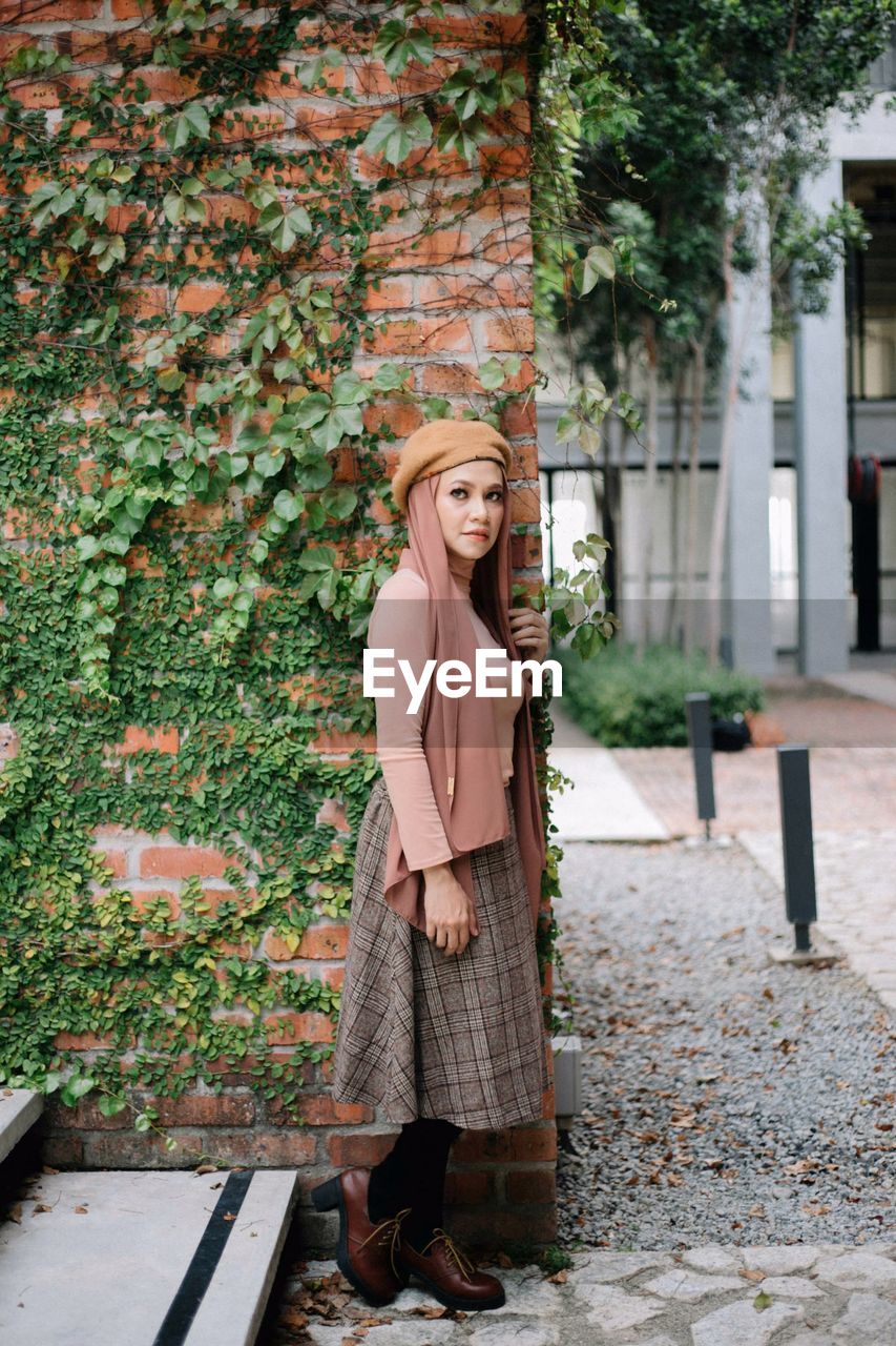 Smiling woman looking away while standing against plants on wall