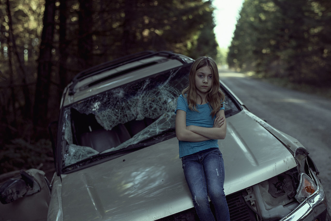 Portrait of girl standing against damaged car