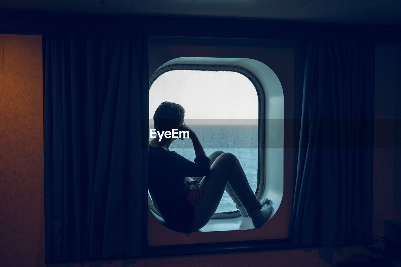 Woman looking at view while sitting at ship window