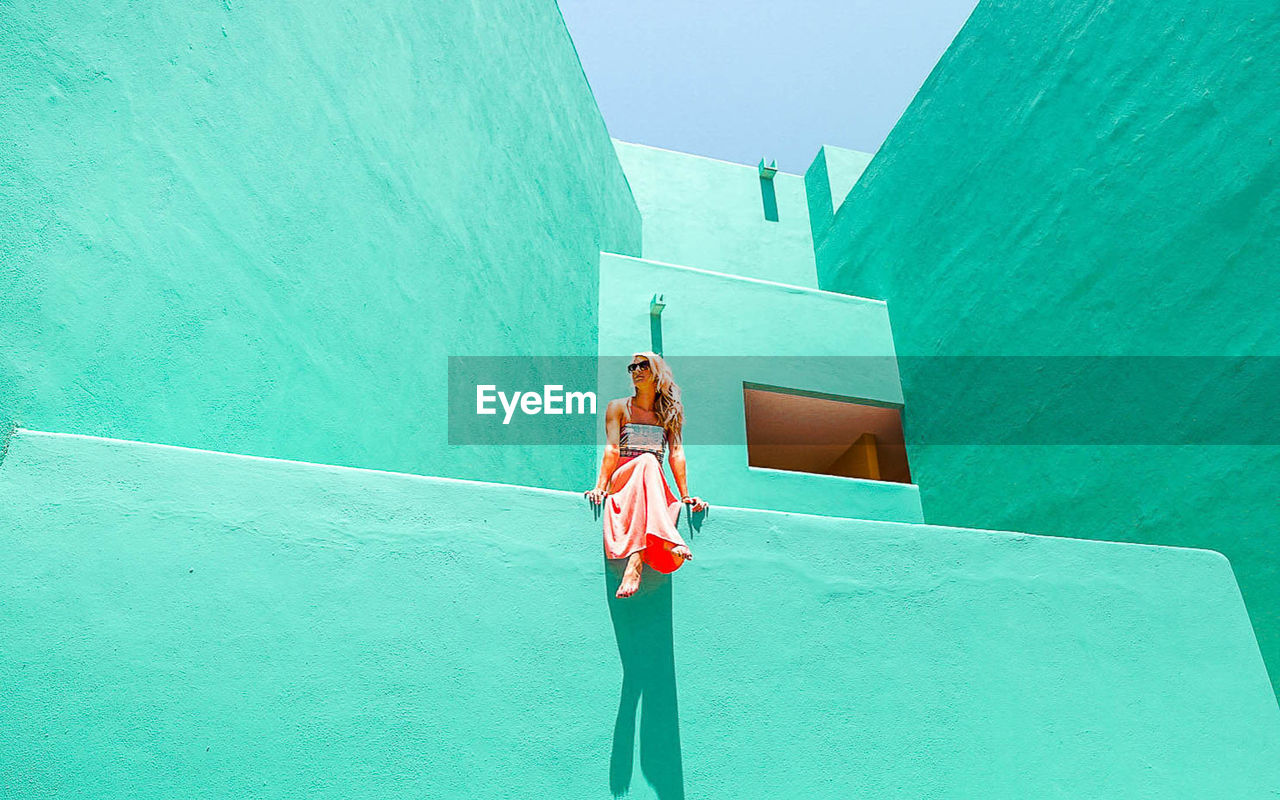 WOMAN WITH UMBRELLA STANDING AGAINST WALL