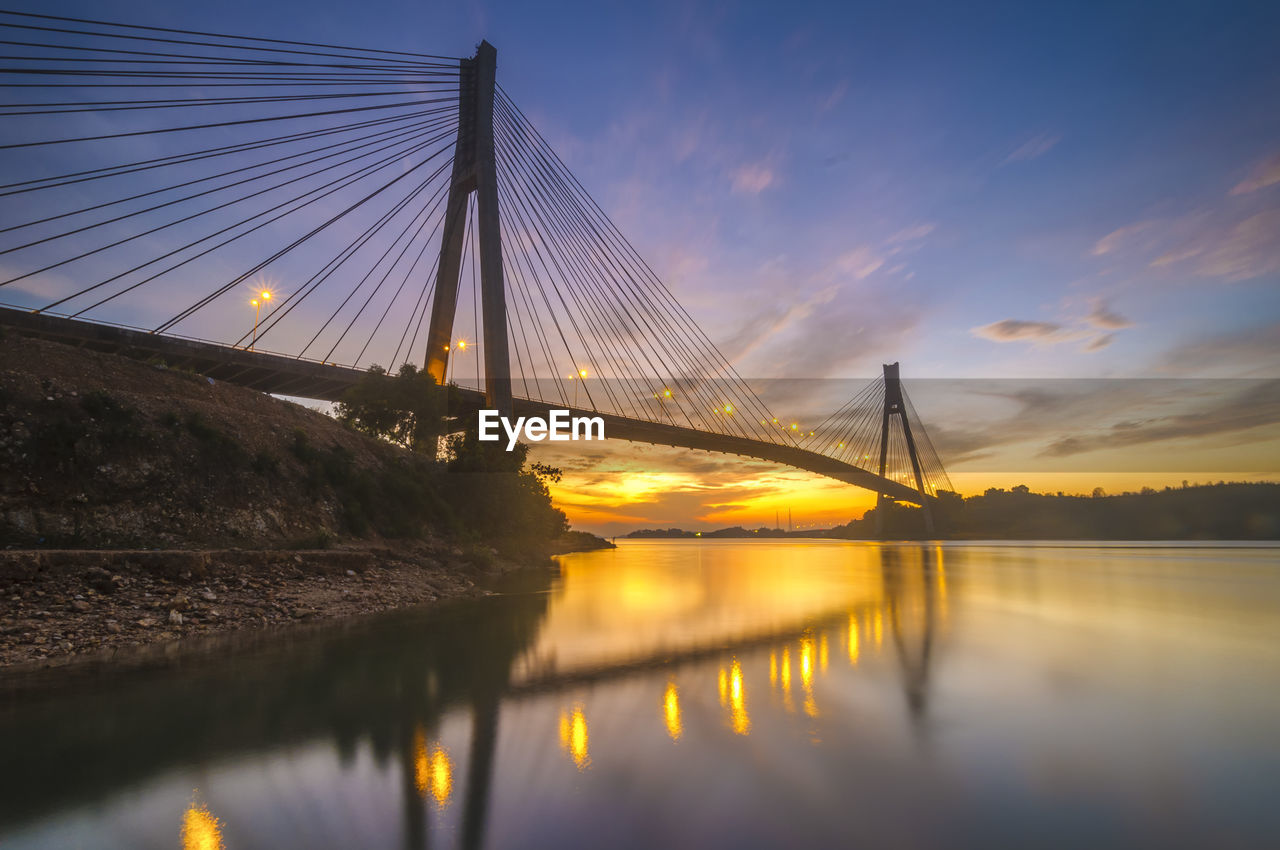 View of suspension bridge over river at sunset