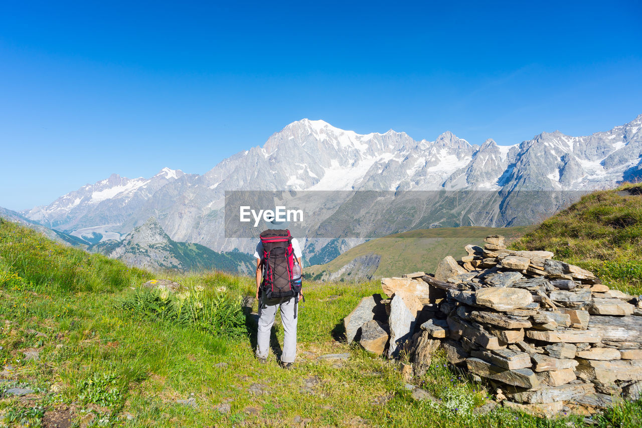 Rear view of backpack hiker standing against mountains in winter