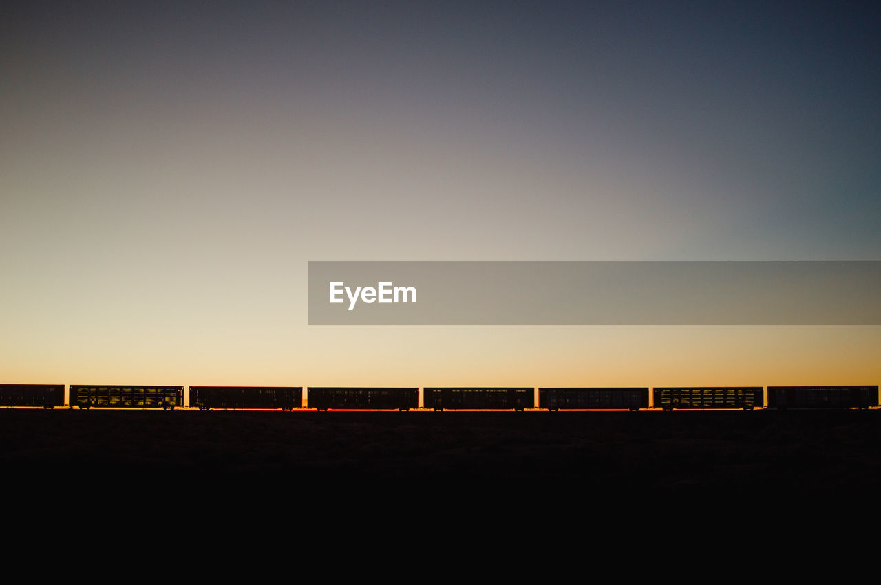 Silhouette freight train against clear sky during sunset