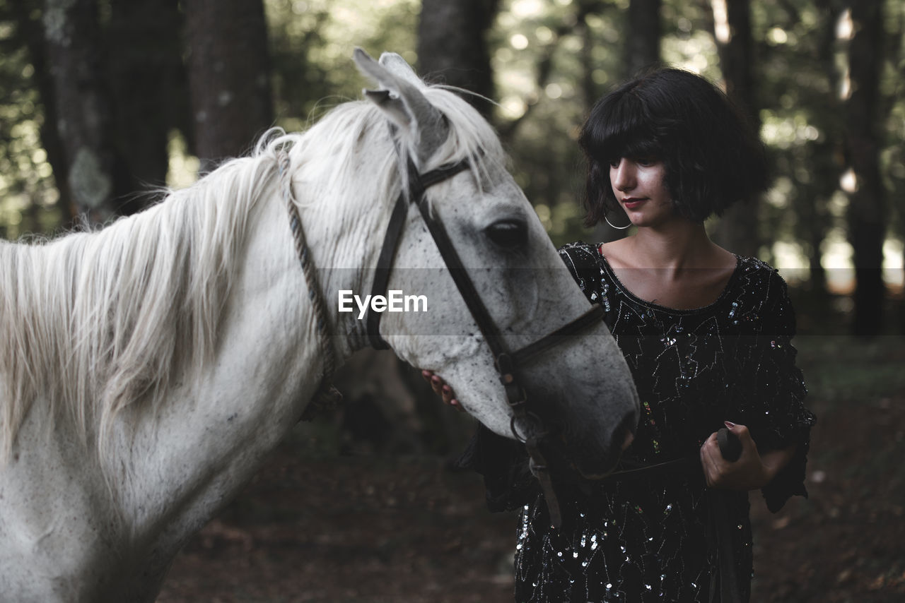 Young woman standing by horse in forest