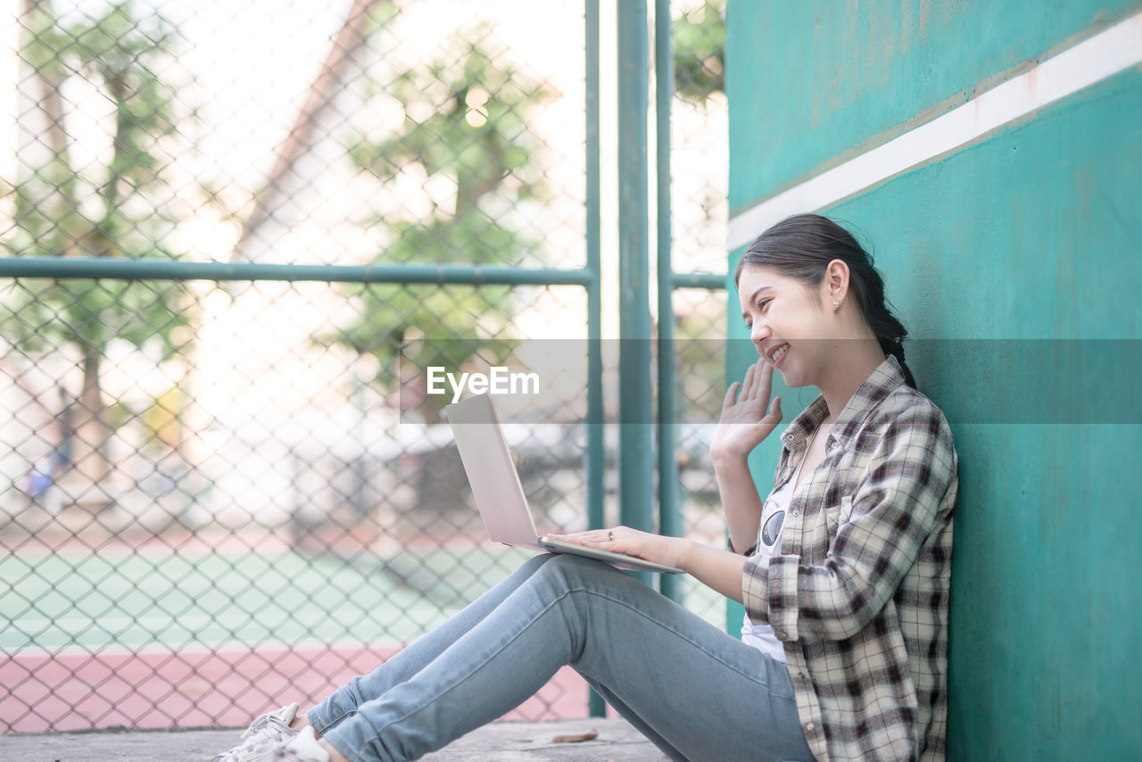 Full length of young woman using laptop at tennis court