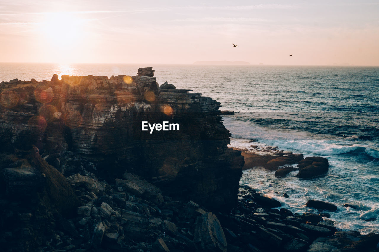 Scenic view of cliff by sea against sky during sunset