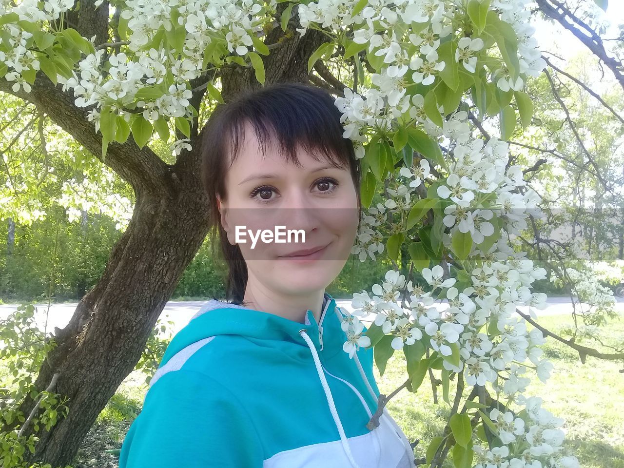 Portrait of young woman standing by white flowers on branch