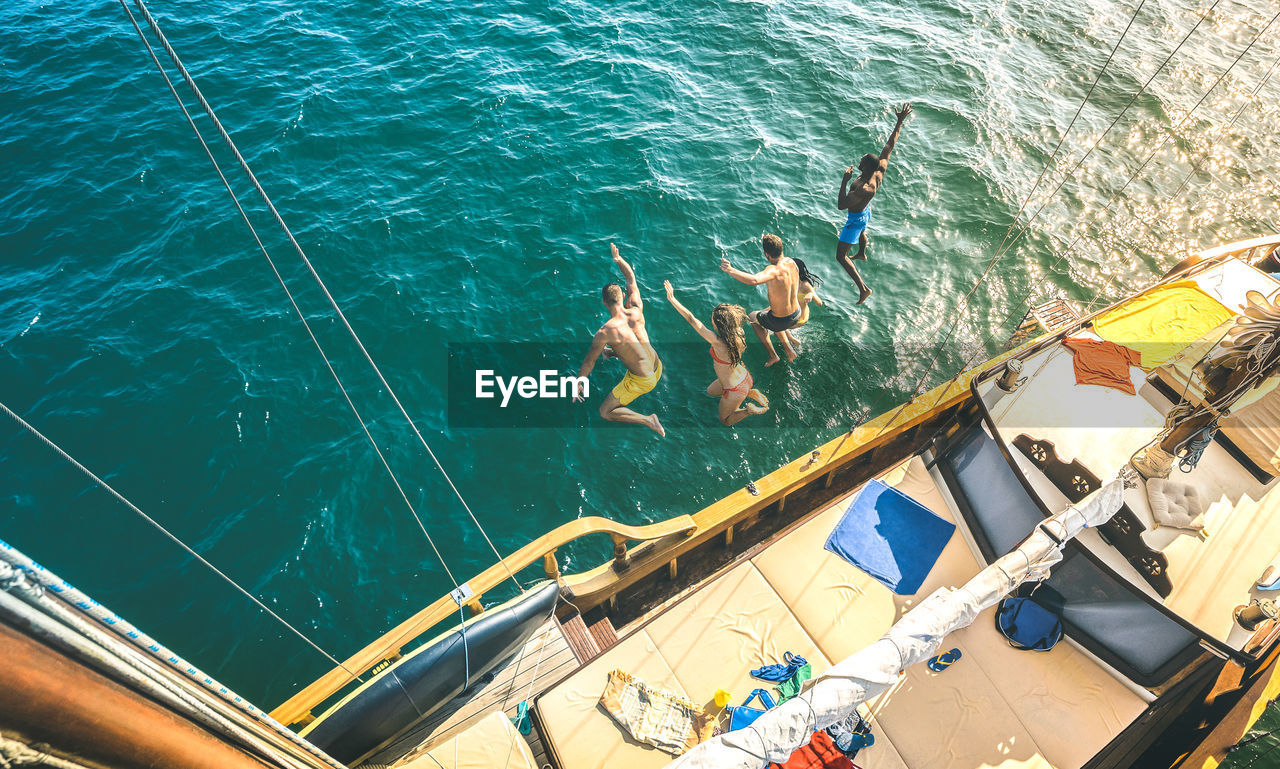 High angle view of friends jumping into sea from sailboat