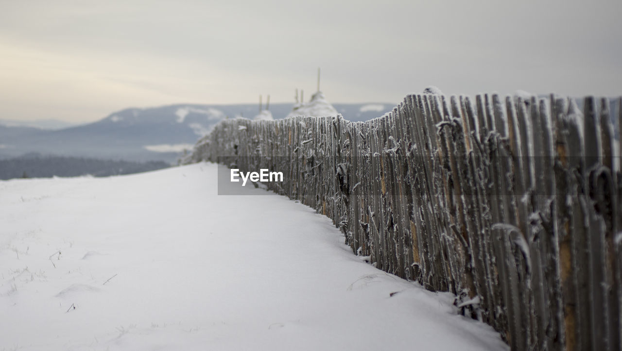 Fence on snow covered field against sky