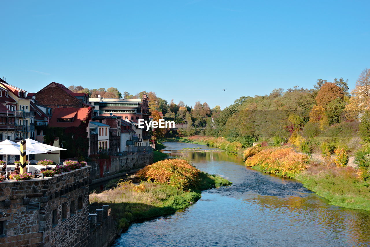 Buildings by river against clear blue sky