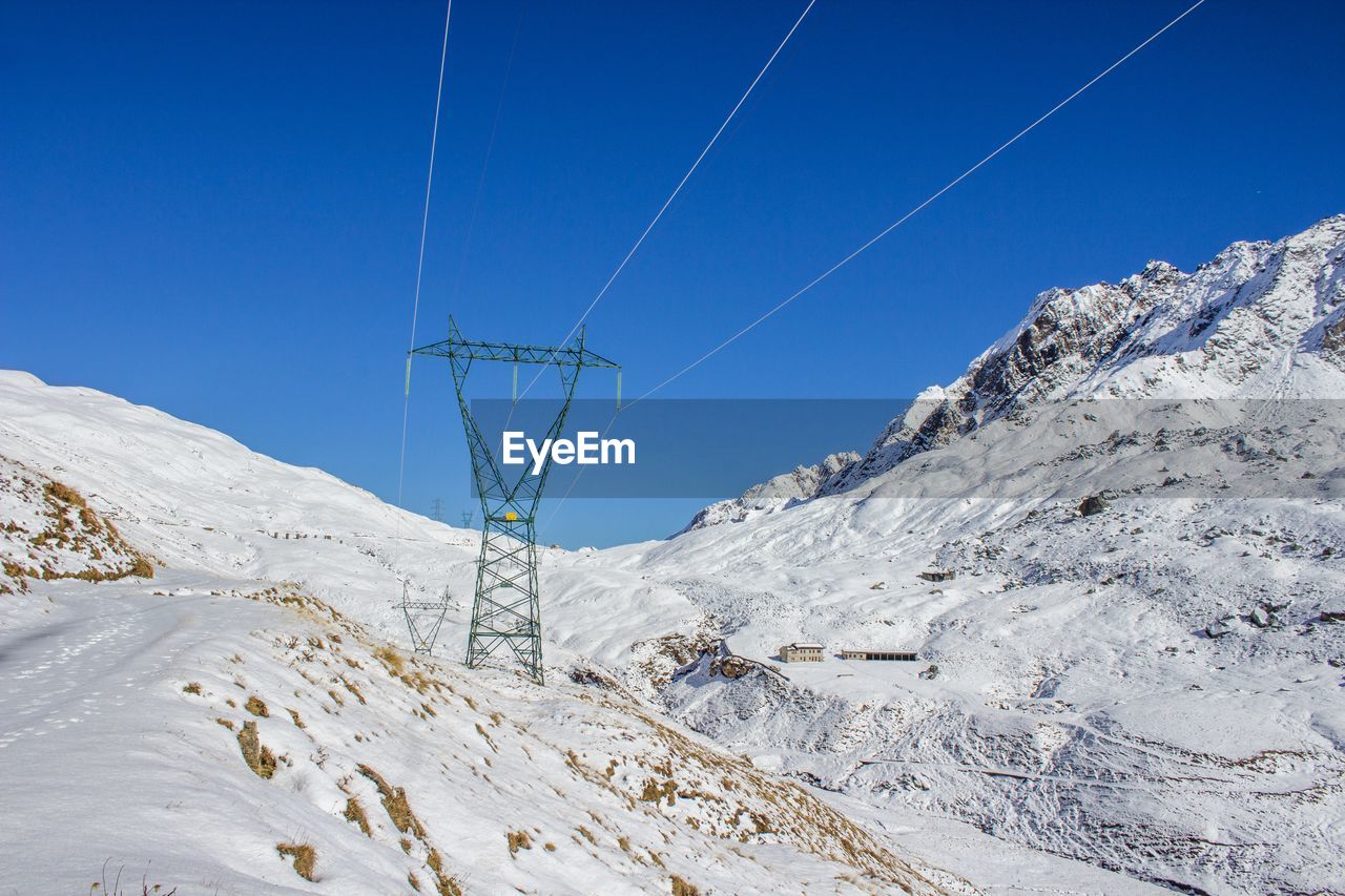 Power line on snow covered mountain against blue sky