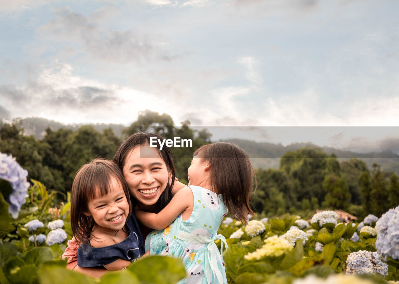 Portrait of smiling mother with cute daughters against sky