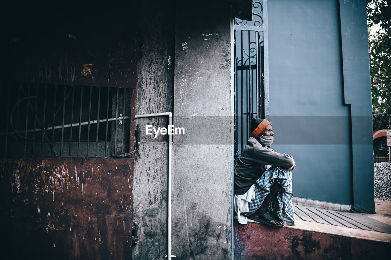 MAN SITTING BY WALL