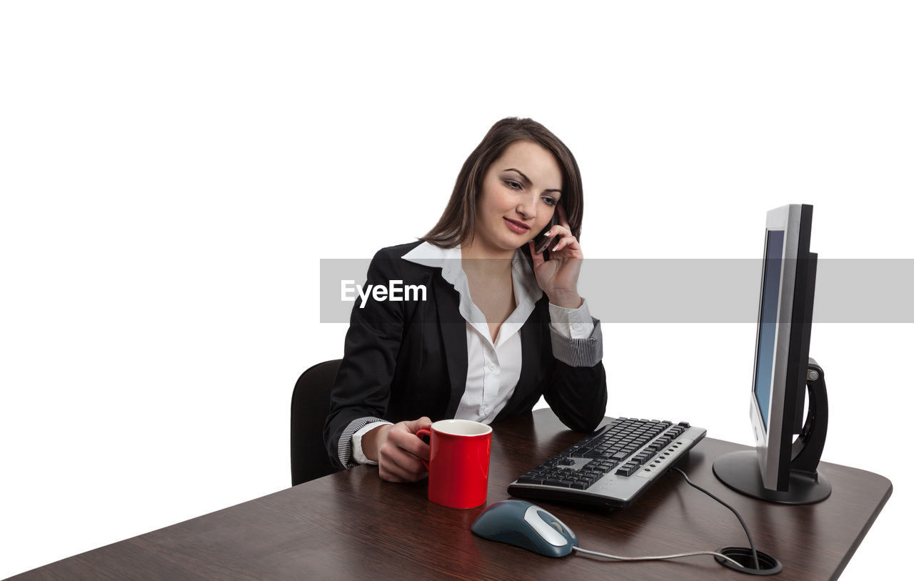 PORTRAIT OF YOUNG WOMAN USING PHONE WHILE SITTING ON TABLE