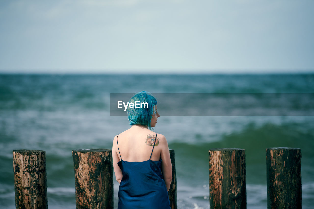 Beautiful blue-haired woman in long dark blue dress with cute tattoo on her shoulder blade