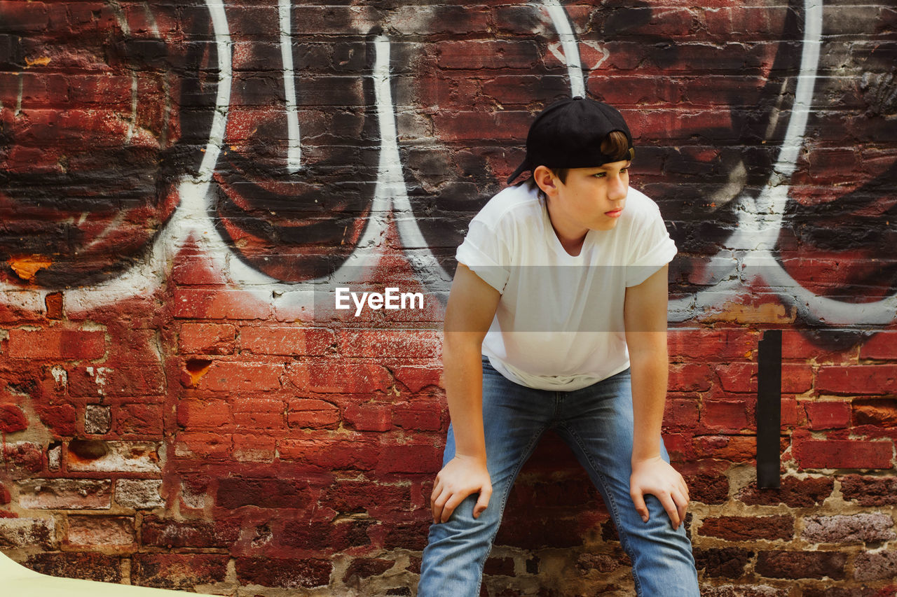 Full length of young man standing against brick wall