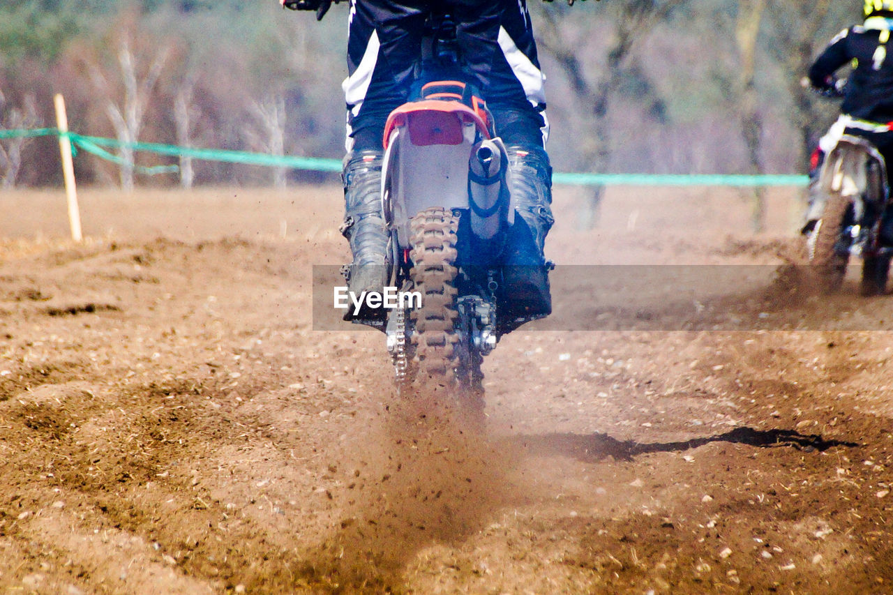 Low section of man riding motorcycle in motocross race on mud