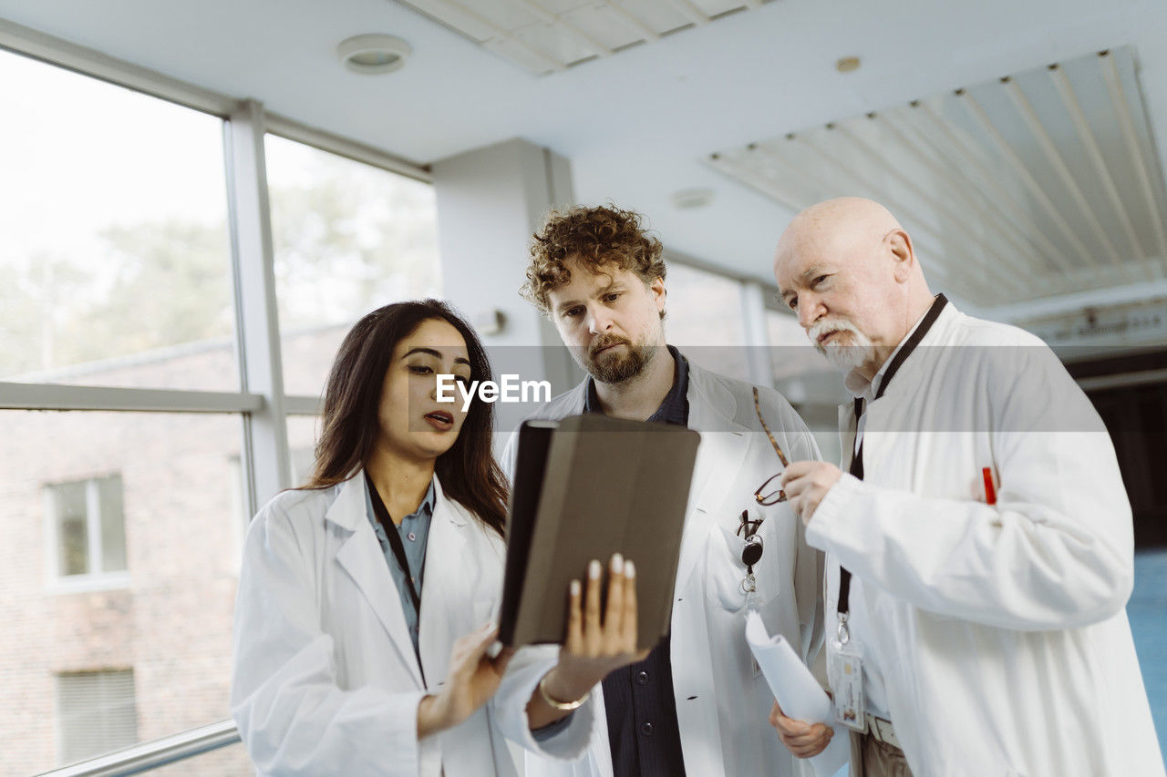 Female doctor discussing over digital tablet with male colleagues in hospital corridor