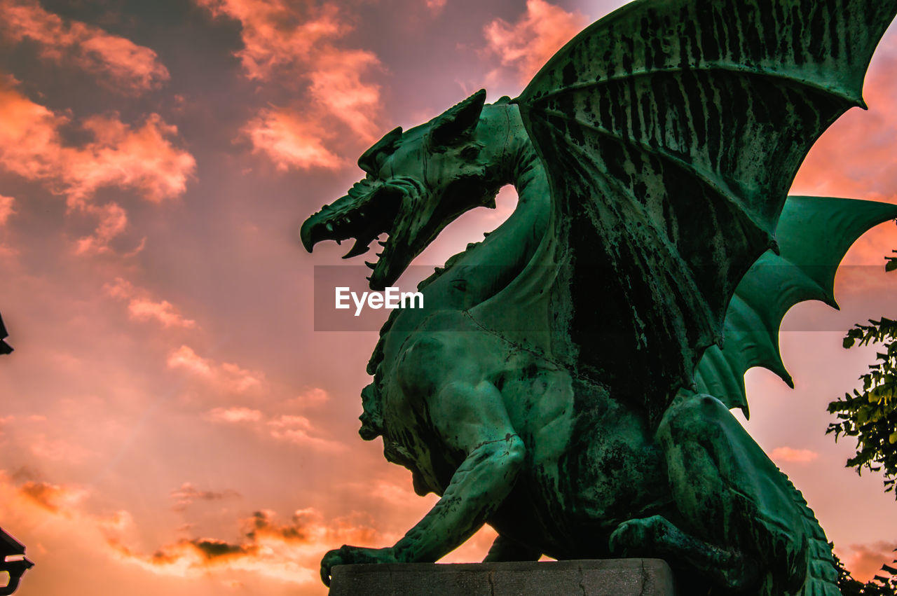 LOW ANGLE VIEW OF STATUE AGAINST ORANGE SKY