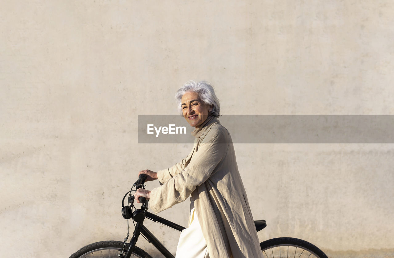 Smiling mature woman on bicycle by wall