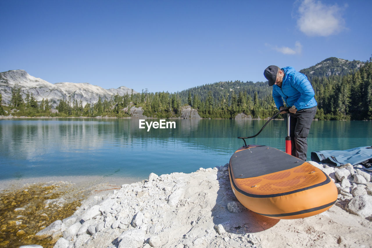 Adventurous man pumps up inflatable sup next to a remote lake.