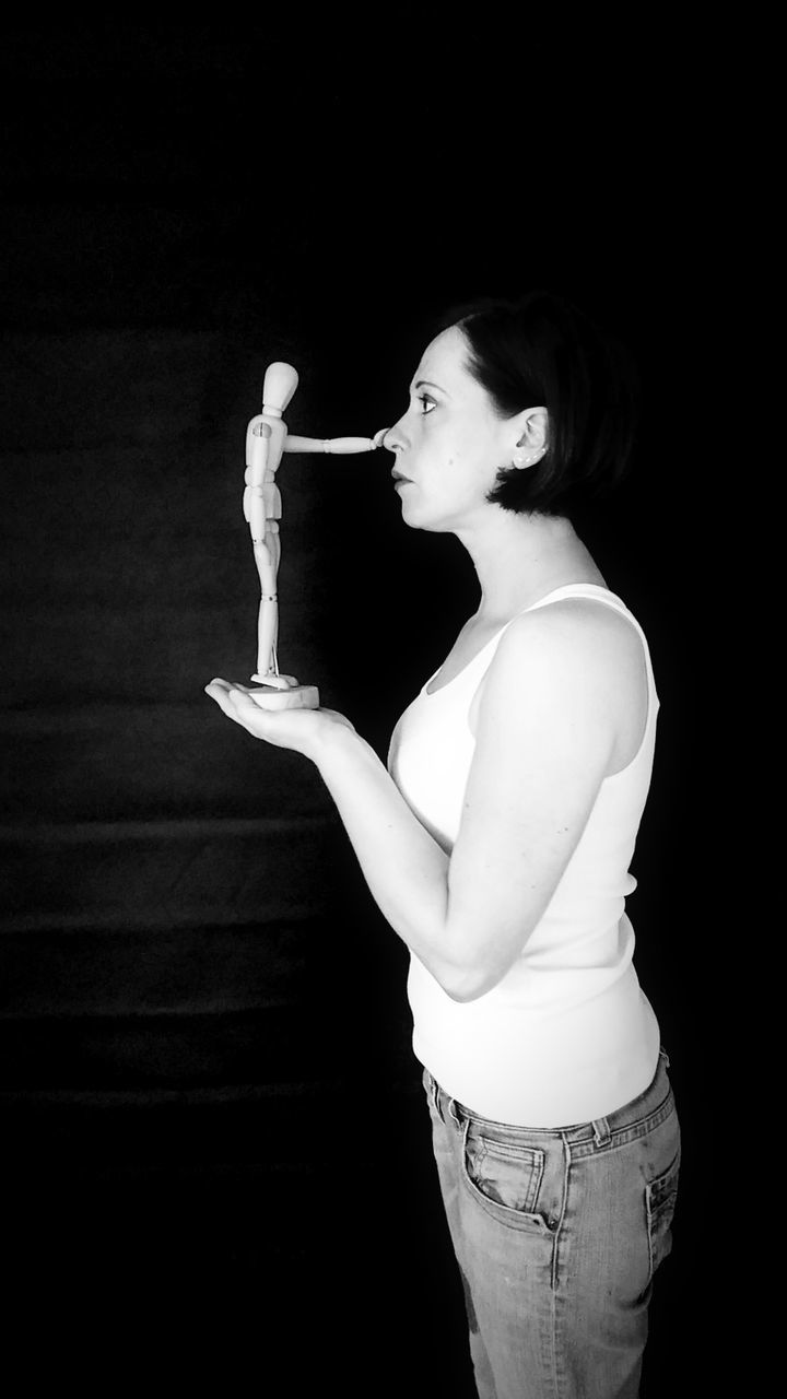 Side view of woman holding figurine against black background