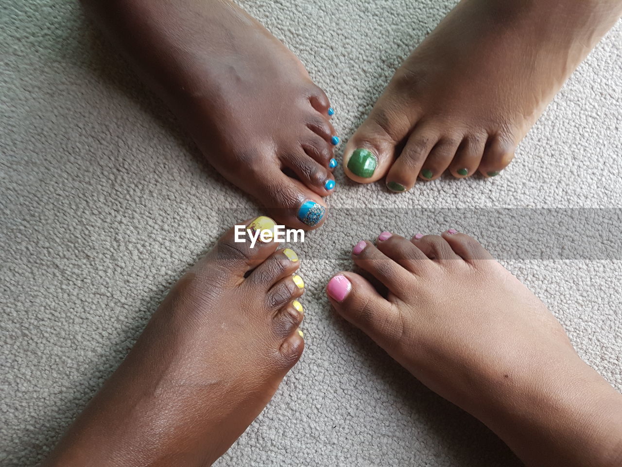 Low section of female friends with colorful nail polishes on carpet