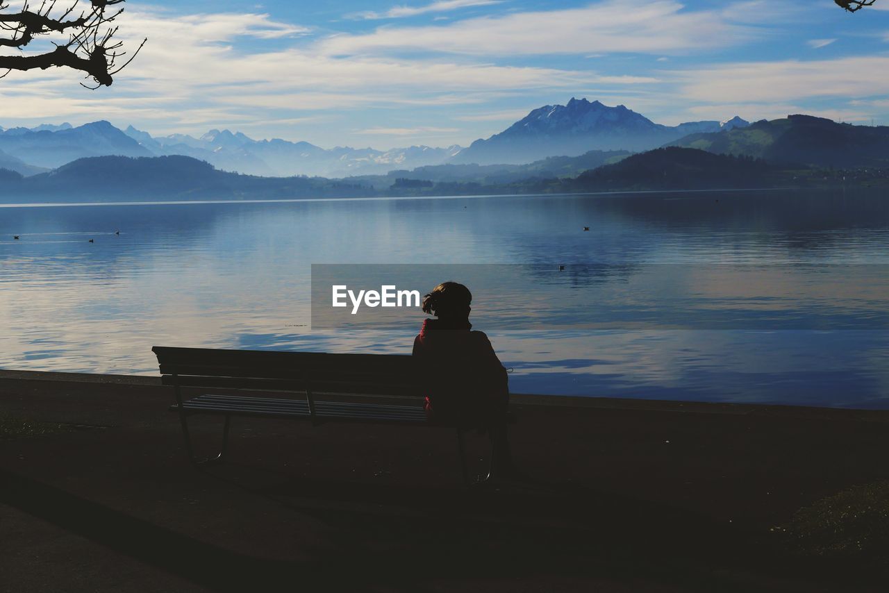 Woman sitting on seat by lake against sky in switzerland 