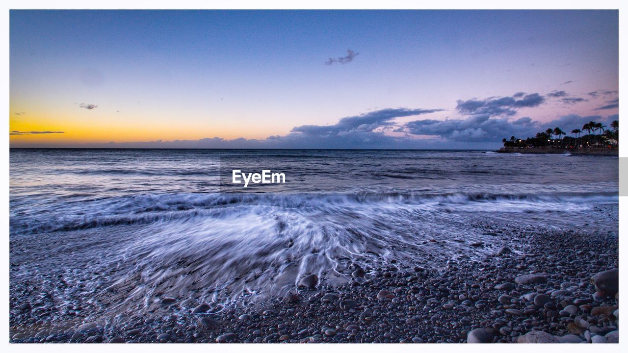 SCENIC VIEW OF BEACH AGAINST SKY AT SUNSET