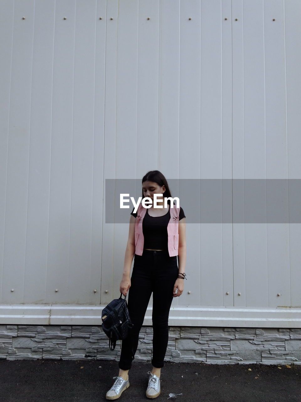 Full length of young woman with backpack standing against wall