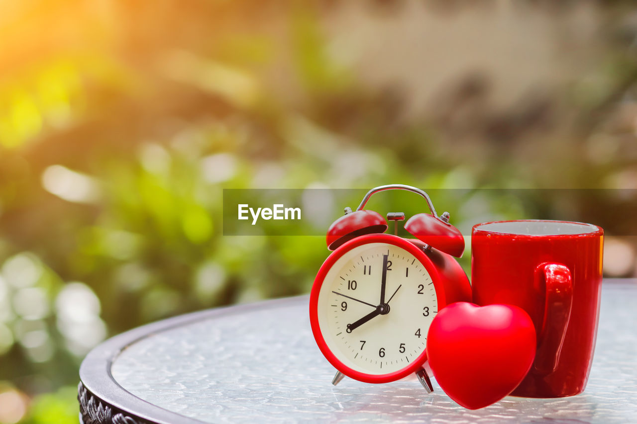 Close-up of clock with cup and heart shape on table