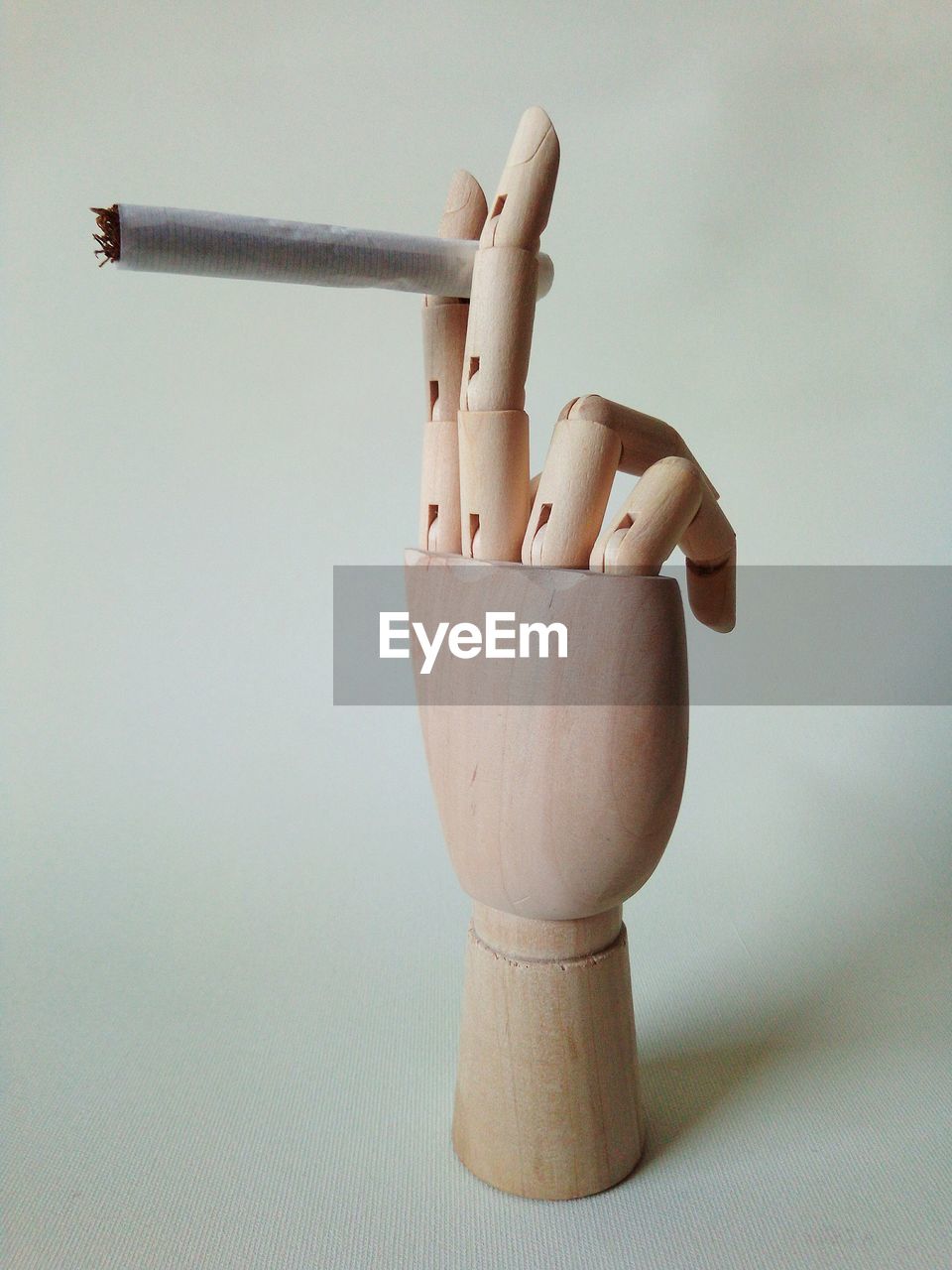Close-up of wooden figurine holding cigarette against white background